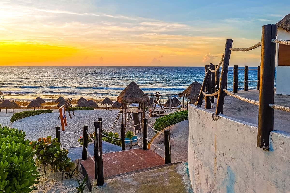 Atardecer sobre una playa de Cancún con palapas de palma y pasarela de madera