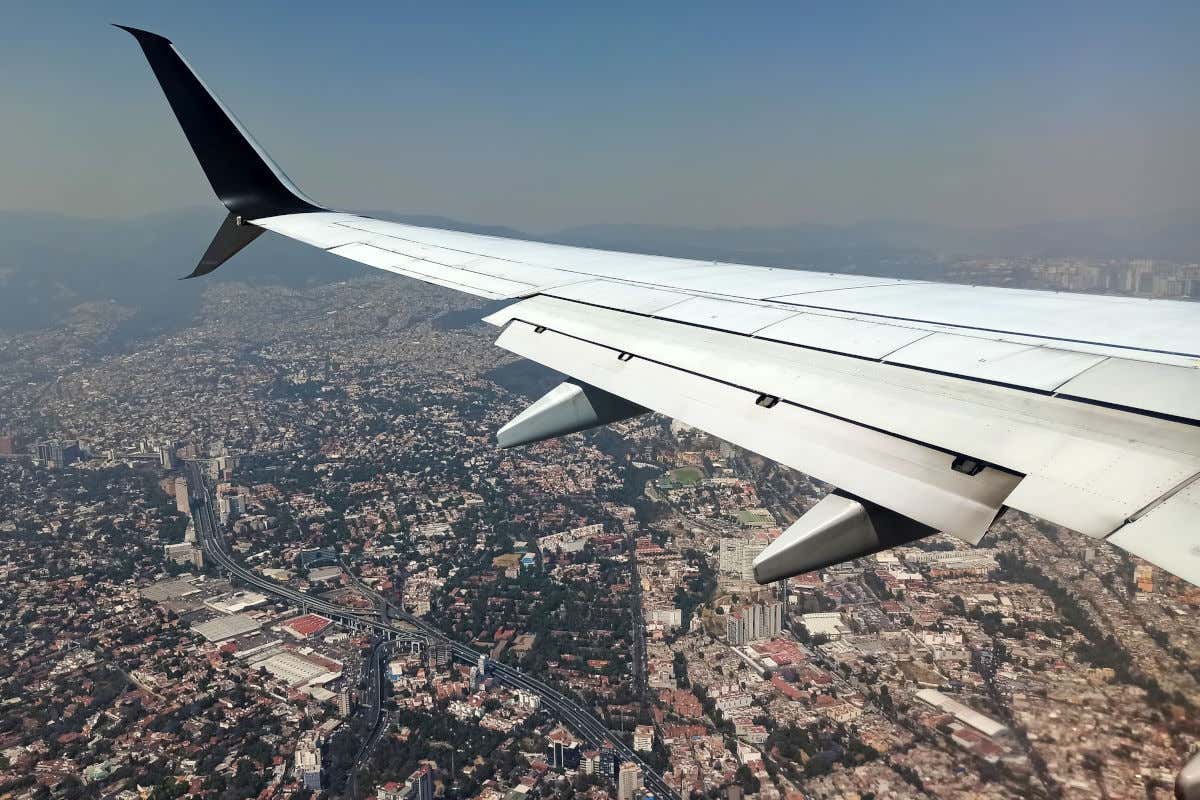 Ala de un avión sobrevolando Ciudad de México repleta de edificios