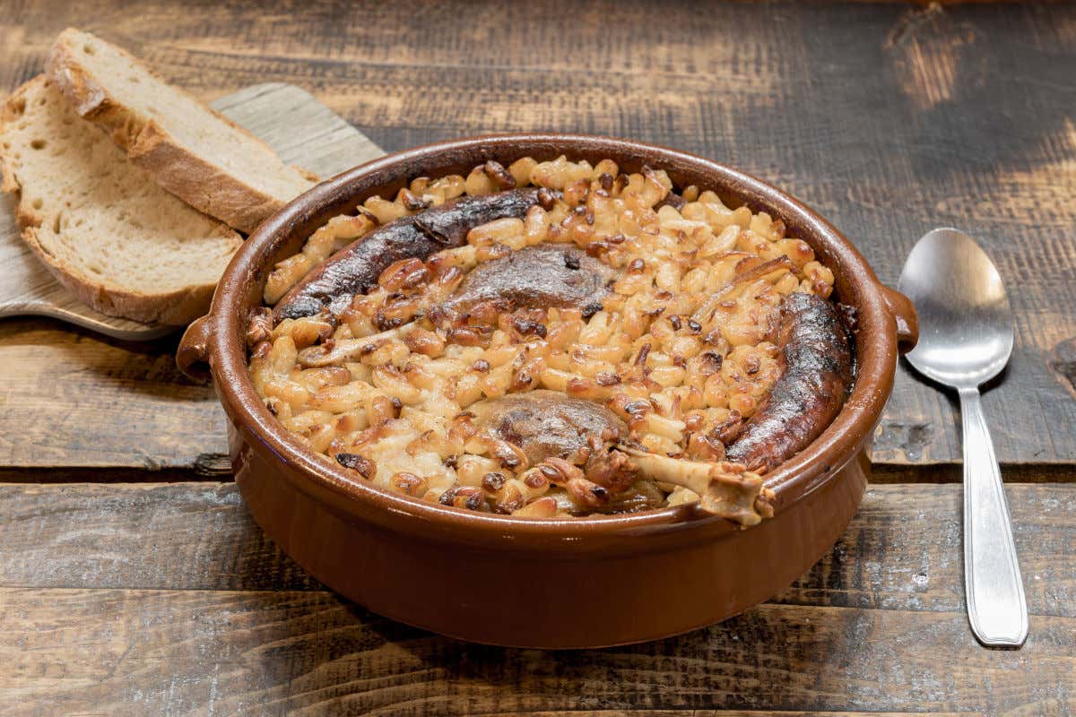 Un recipiente de barro con cassoulet, un guiso tradicional francés con alubias, salchichas y carne de pato