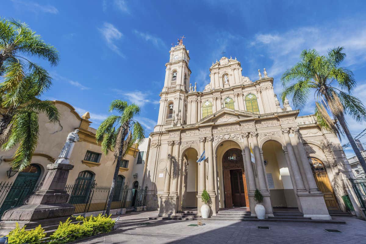 Una plaza con una escultura de un santo junto a la fachada de la catedral de San Salvador de Jujuy en un día despejado