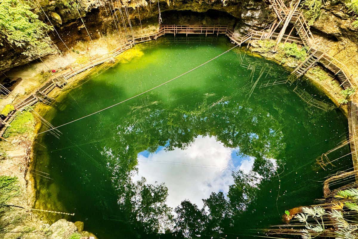 Vista aérea del cenote Xcanché reflejando en sus aguas esmeralda la frondosa vegetación que lo rodea