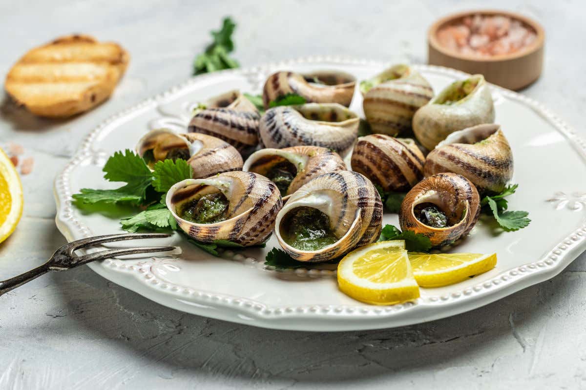 Un plato de escargots de Bourgogne o caracoles de Borgoña rellenos de salsa de perejil y mantequilla y acompañados por unas rodajas de limón
