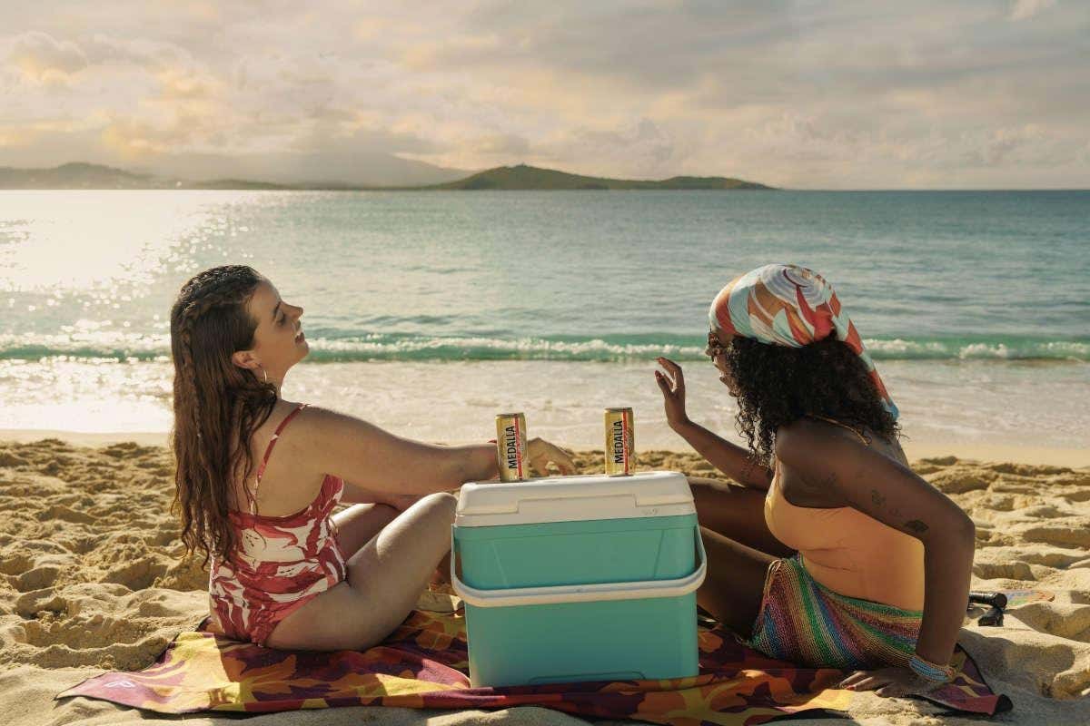 Dos chicas junto a una nevera sentadas en la arena de la playa al atardecer