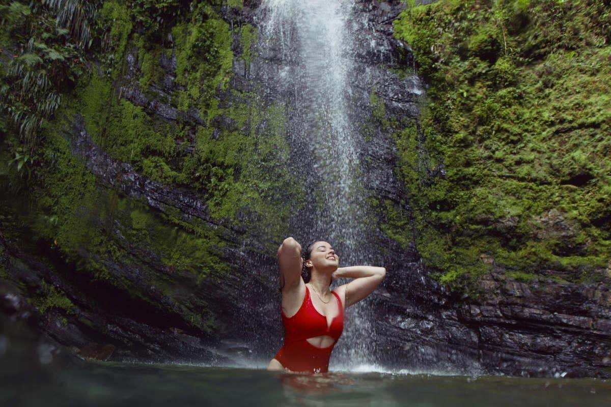 Una chica con bañador rojo bañándose en una cascada