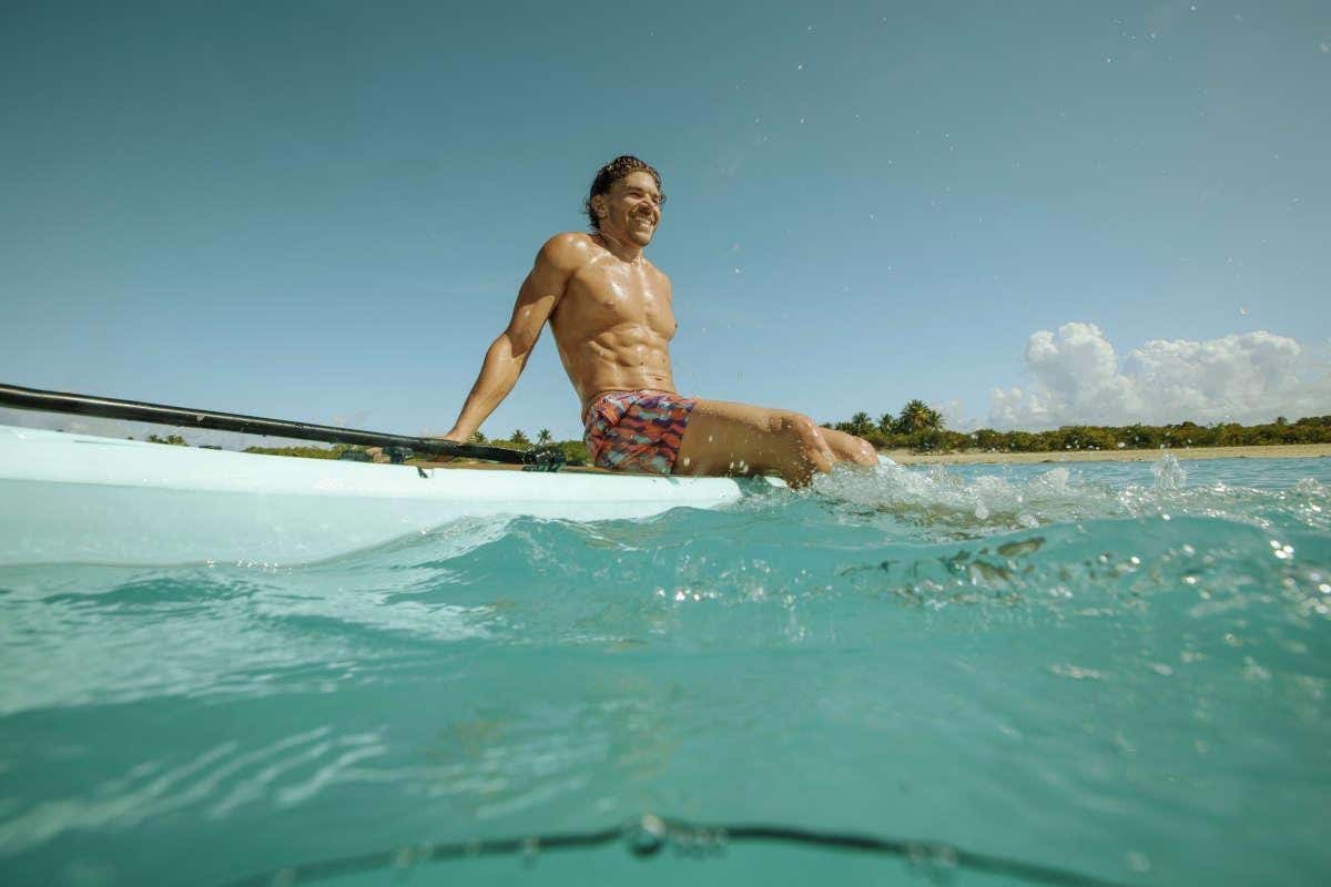 Un chico en bañador sentado sobre una tabla de surf en una playa del Caribe