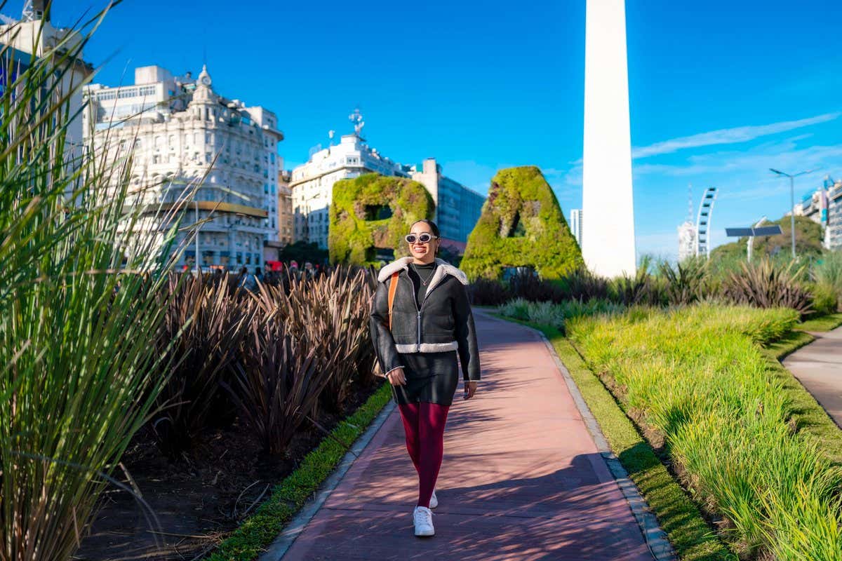 Turista con abrigo paseando junto al Obelisco de Buenos Aires en un día soleado de cielo despejado