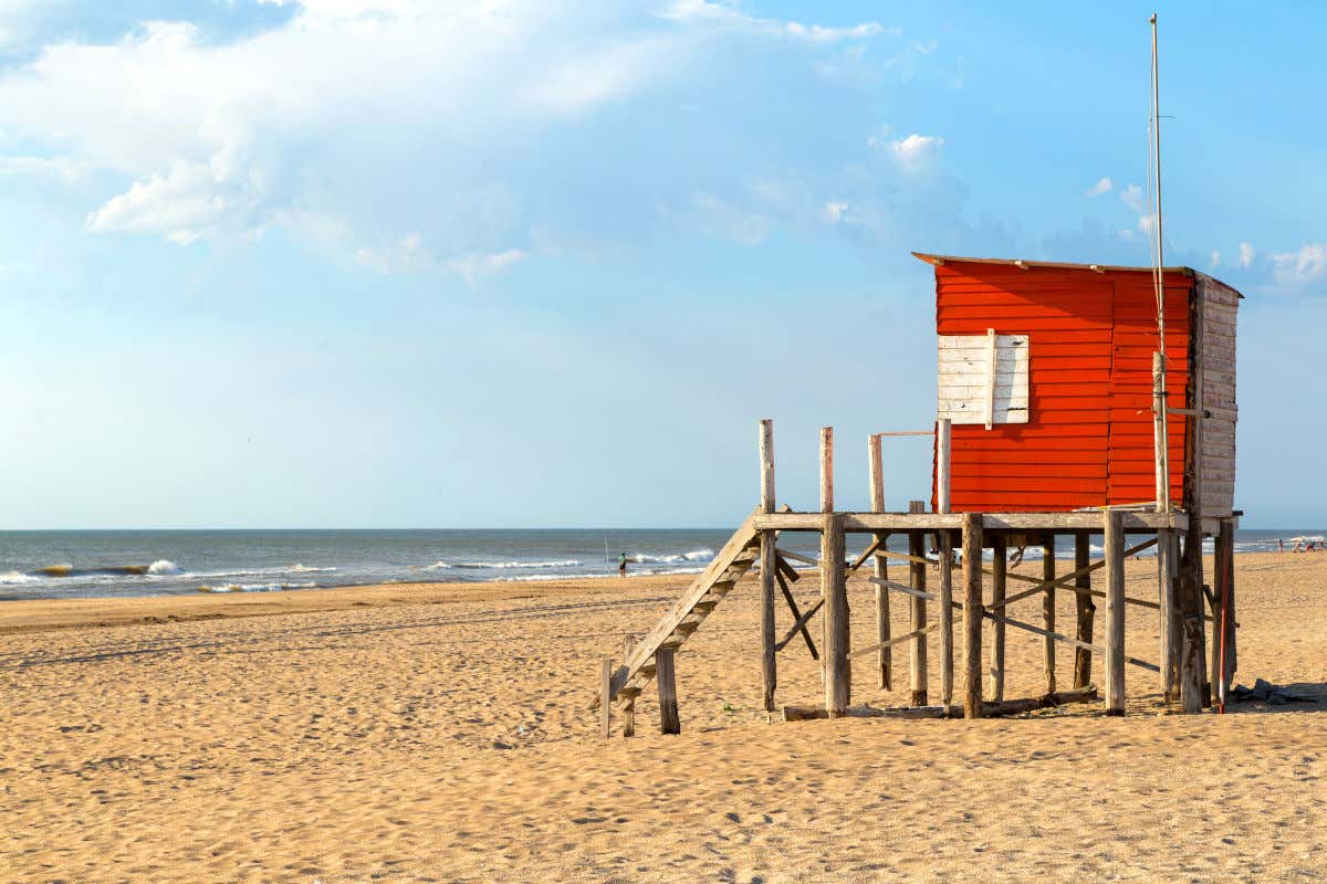A golden sand beach at Mar de las Pampas in Argentina with a red wooden lifeguard hut