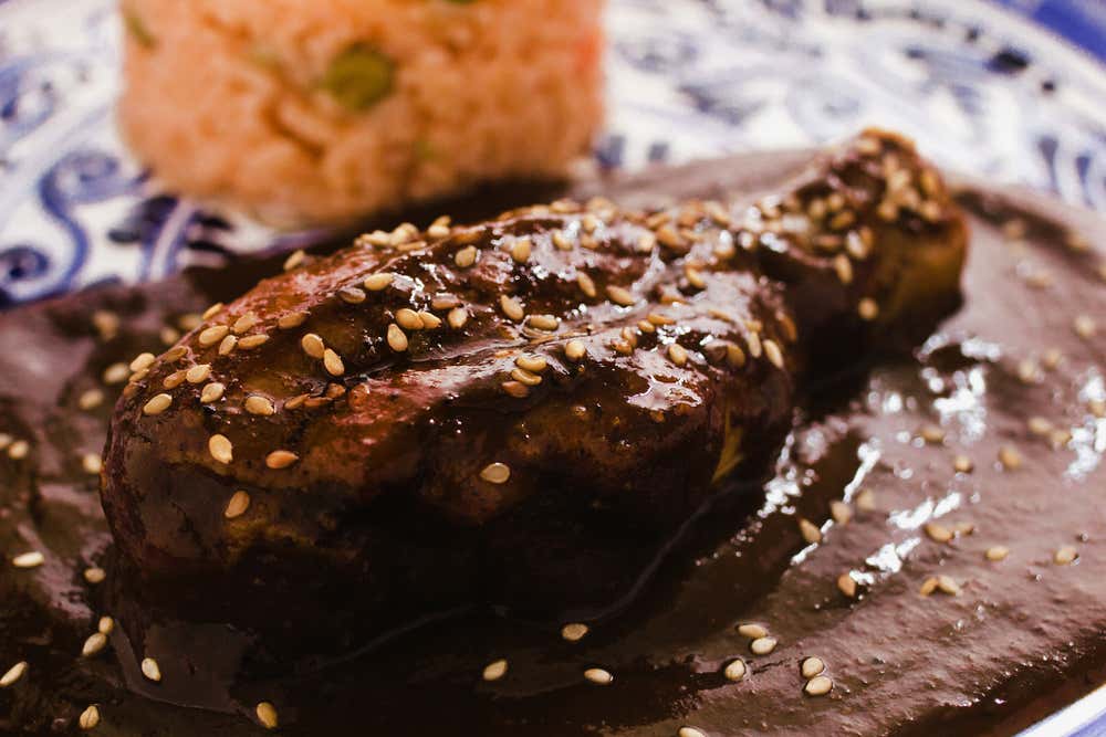 A close-up of Mole Poblano, a thick brown sauce served over chicken with seeds on top.