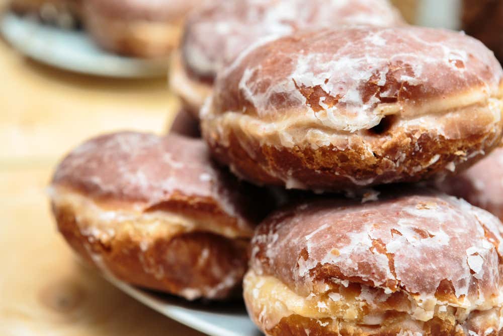 Primo piano di una pila di pączki tradizionali polacchi, lievitati e fritti, ricoperti da una sottile glassa di zucchero lucida e leggermente crepata