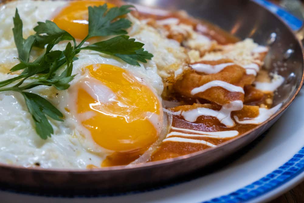 A close-up of chilaquiles served with red sauce and eggs.