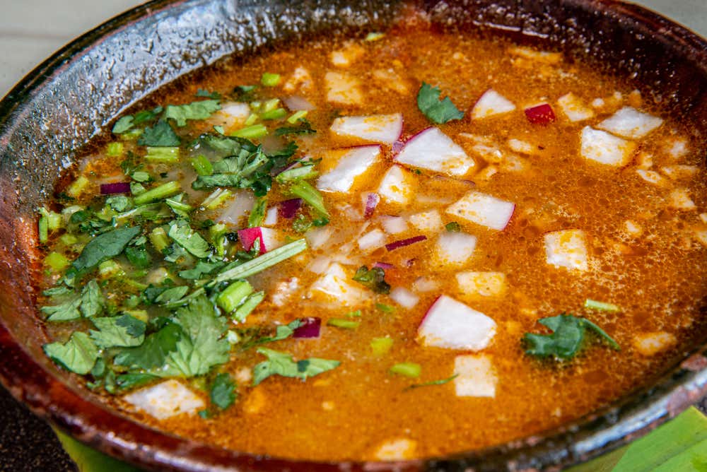 A close-up of Birria broth with various toppings including cilantro and onions.