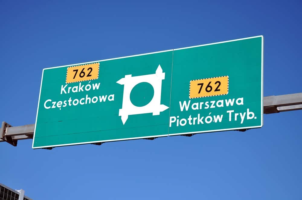 Cartello stradale autostradale verde in Polonia che indica le direzioni della strada 762 verso Kraków e Częstochowa a sinistra, e Warszawa e Piotrków Tryb. a destra, sotto un cielo blu terso.