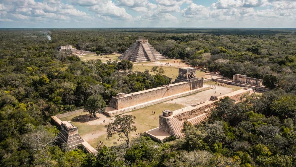 Aerial view of Chichén Itzá with a cloudy blue sky in the background.