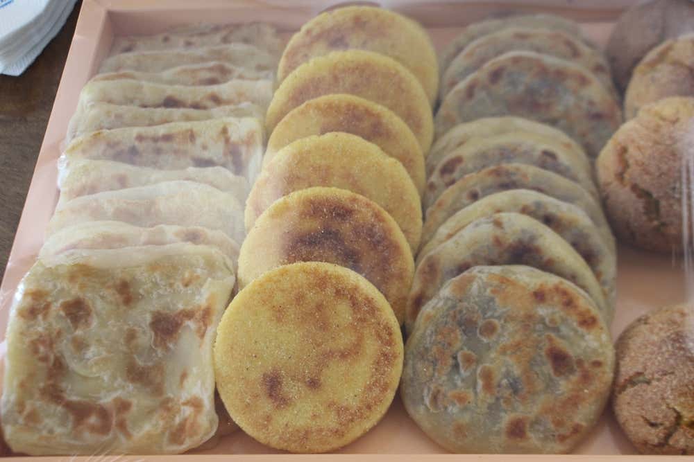 Bandeja con una amplia selección de panes y tortas tradicionales marroquíes dispuestos en filas ordenadas: hojas cuadradas de msemen doradas a la izquierda, panecillos redondos de harcha de sémola en el centro y batbout o pan árabe redondo y dorado a la derecha