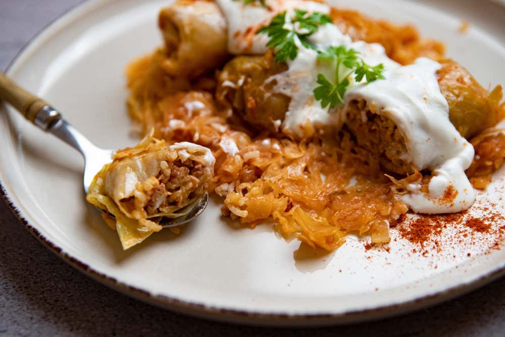 Involtini di cavolo ripieni di carne e riso serviti su un letto di cavolo cappuccio, guarniti con panna acida, prezzemolo fresco e una spolverata di paprika, con un boccone infilzato su una forchetta in primo piano