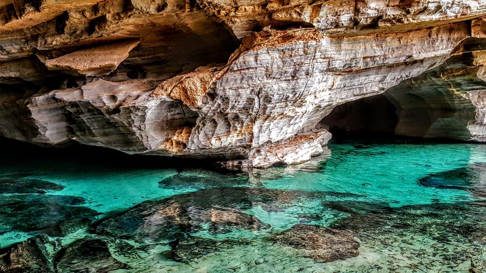 Gruta com lagoa de águas cristalinas no Parque Nacional da Chapada Diamantina, na Bahia, Brasil, destacando as formações rochosas e os impressionantes tons de azul da água iluminada pela luz natural