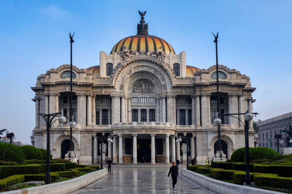 The front of the Palacio de Bellas Artes with its brighr orange and yellow dome, with a clear blue sky in the background.