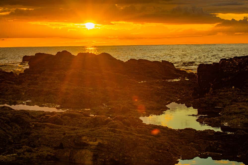 Pôr do sol em Jericoacoara, no Ceará, Brasil, com raios dourados iluminando as formações rochosas à beira-mar e criando uma paisagem serena em um dos cenários mais emblemáticos do litoral brasileiro
