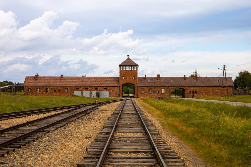 Vista prospettica dei binari ferroviari che conducono verso la porta d'ingresso principale e la torre di guardia in mattoni mattoni rossi (la "Porta della Morte") del campo di sterminio di Auschwitz II-Birkenau