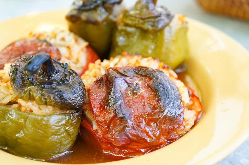 Piatto fondo giallo contenente gemista tradizionali greche, ovvero pomodori e peperoni verdi ripieni di riso ed erbe aromatiche, cotti al forno con le loro calotte leggermente bruciacchiate