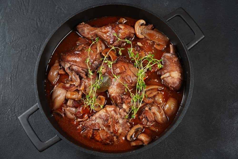 Coq au vin, clássico da culinária francesa, preparado com frango cozido lentamente em vinho tinto, toucinho, cogumelos e cebola