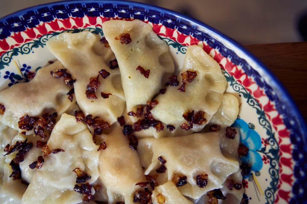 Piatto in ceramica decorata contenente una porzione di pierogi polacchi bolliti, conditi in superficie con pezzetti di cipolla soffritta e pancetta croccante