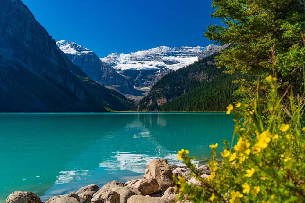 Banff National Park, Alberta seen from a lakeside, with snowy mountains and a clear sky in thebackground.