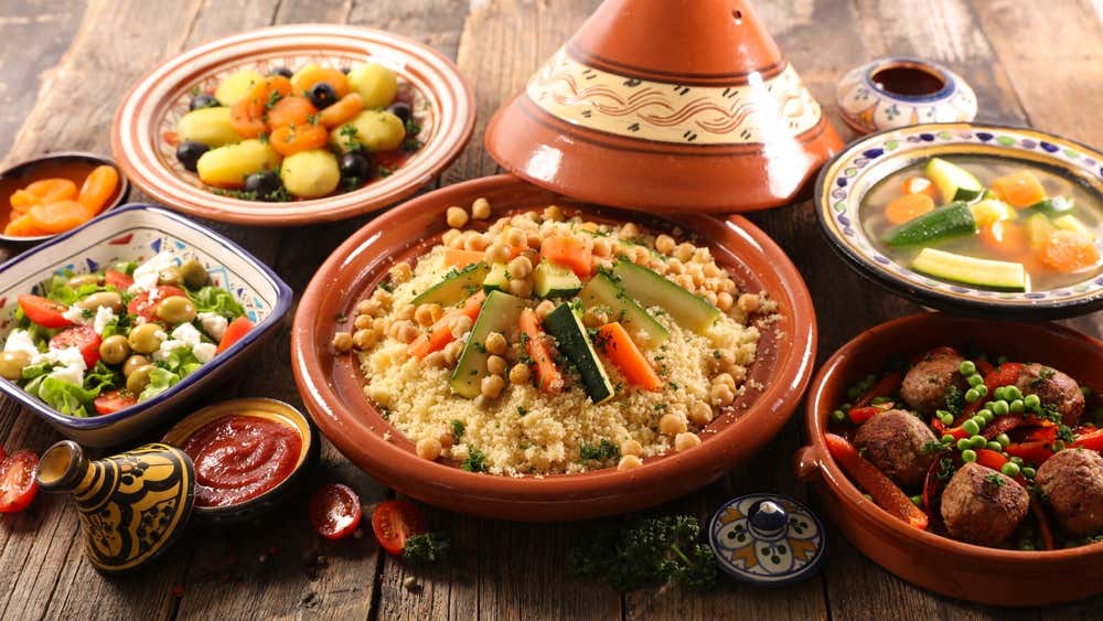 Detalhe de uma mesa com variedade de pratos da cozinha marroquina: tagines, cuscuz e outras especialidades tradicionais