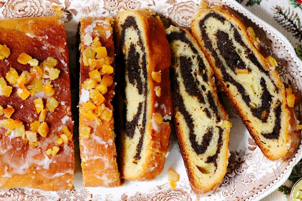 Vista dall'alto di un makowiec polacco affettato su un piatto di ceramica decorato: un rotolo dolce di pasta lievitata farcito con una ricca spirale di semi di papavero scuri, ricoperto di glassa e scorzette d'arancia candite