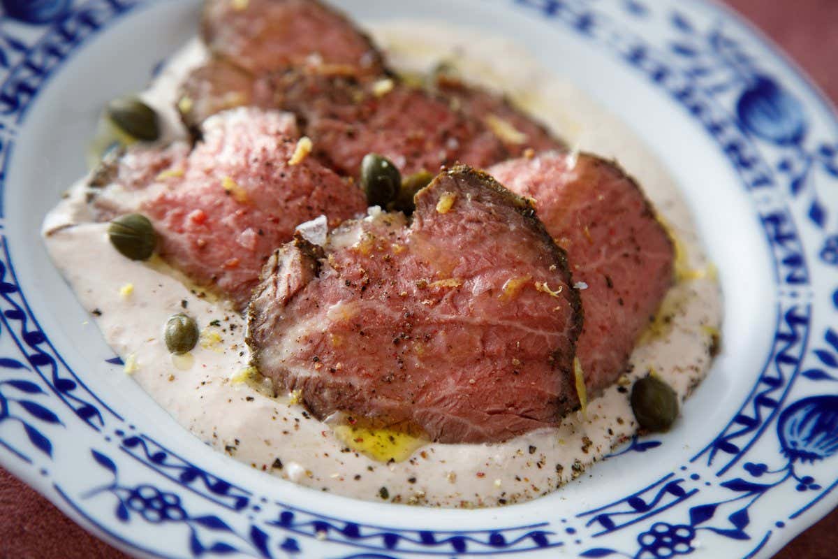 Lonchas de roast beef poco hecho sobre salsa cremosa con alcaparras en un plato decorado