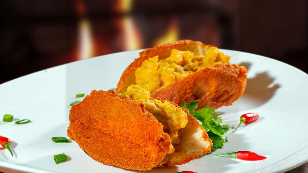Acarajé, tradicional iguaria da culinária baiana, servido em um prato branco. Feito com massa de feijão-fradinho frita no azeite de dendê e recheado com vatapá, camarão seco, vinagrete e pimenta, é um dos símbolos gastronômicos da Bahia