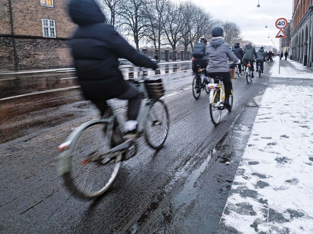 Un gruppo di persone in abiti invernali sfrecciano in bici lungo una strada innevata di Copenaghen