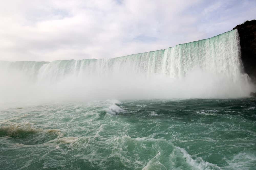Niagara Falls plunging into the water below, and a cloudy sky in the background.