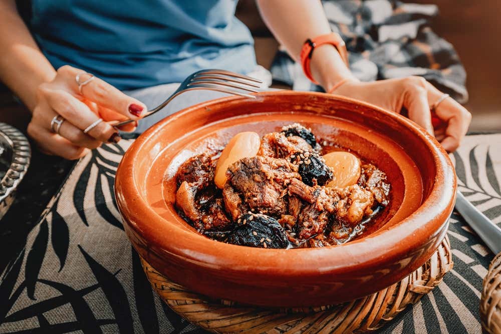 Detalhe de um delicioso tajine com carne de cordeiro cozida lentamente, ameixas, damascos secos e sementes de gergelim, servido em um prato tradicional de terracota