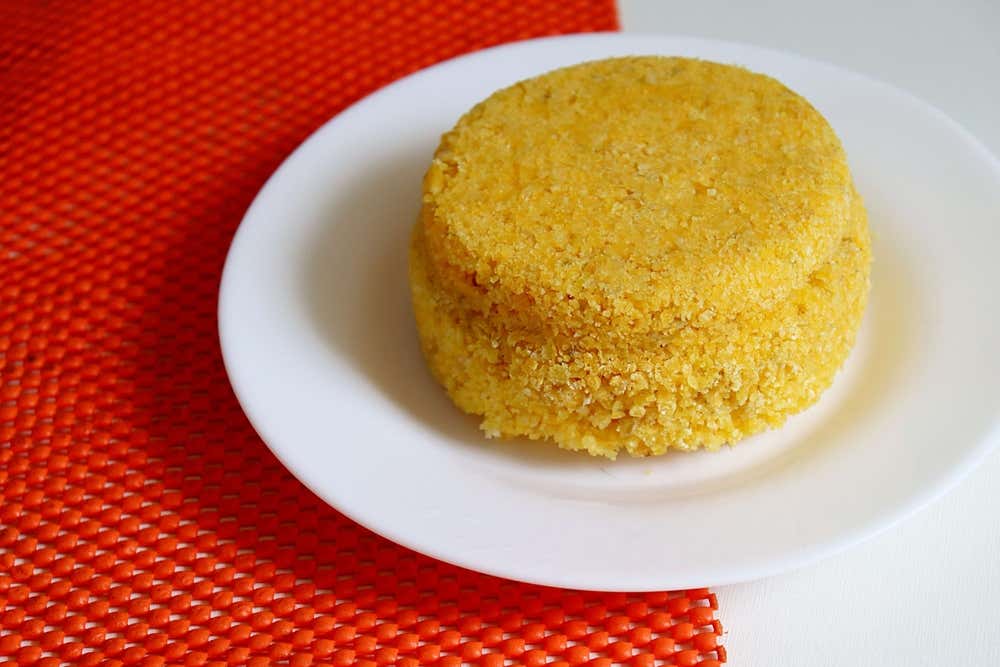 Cuscuz nordestino servido em prato branco, preparado com flocos de milho e acompanhado de ingredientes típicos da culinária brasileira