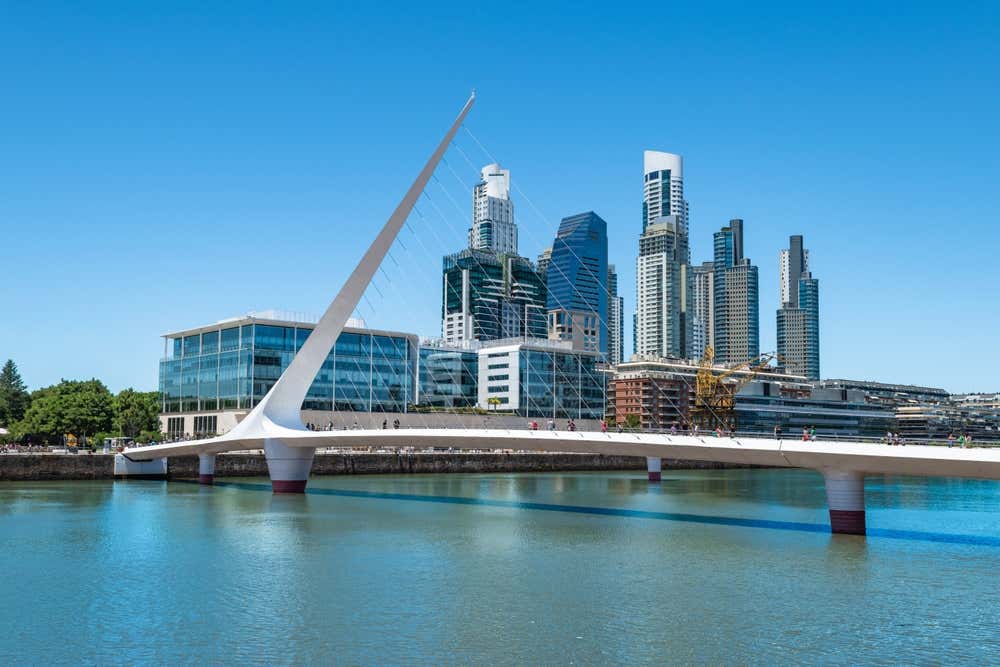 Vista de Puerto Madero, em Buenos Aires, com a Ponte da Mulher sobre as águas calmas e o céu azul ao fundo