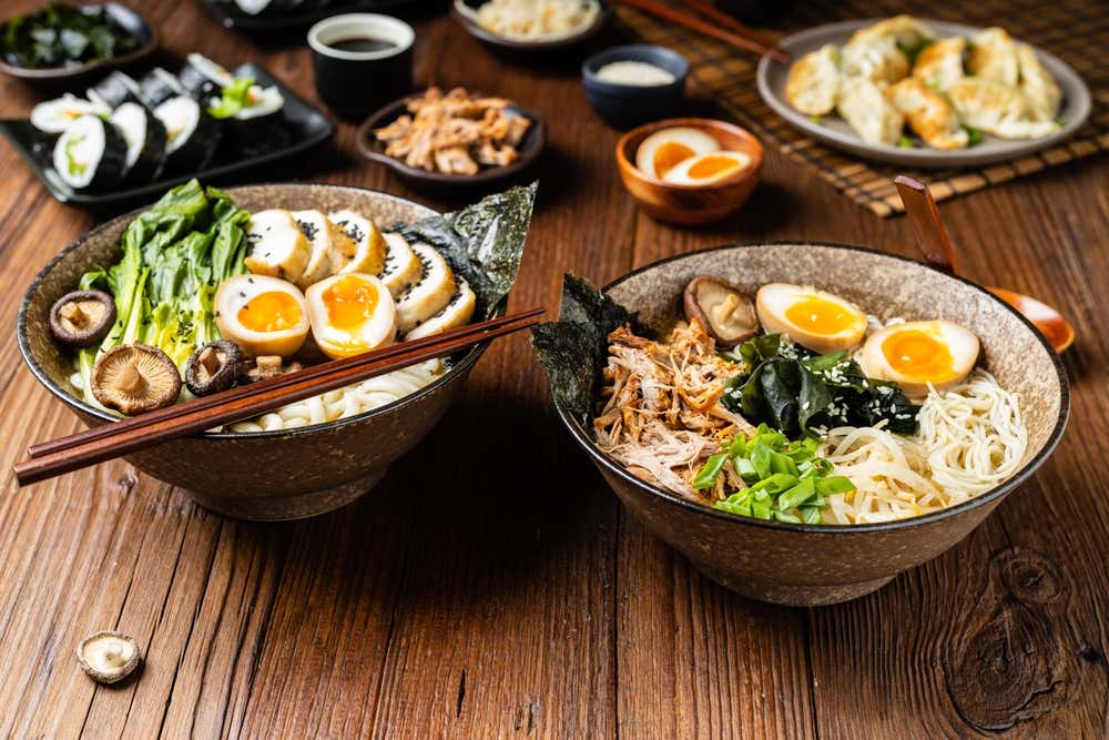 Ramen tradicional com carne de porco ou frango, macarrão e cogumelos, servido em uma tigela clássica, acompanhado de gyozas sobre uma mesa de madeira