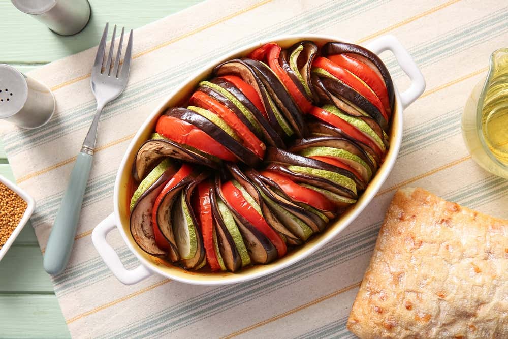 Ratatouille assado no forno, servido em um prato sobre uma superfície de madeira verde