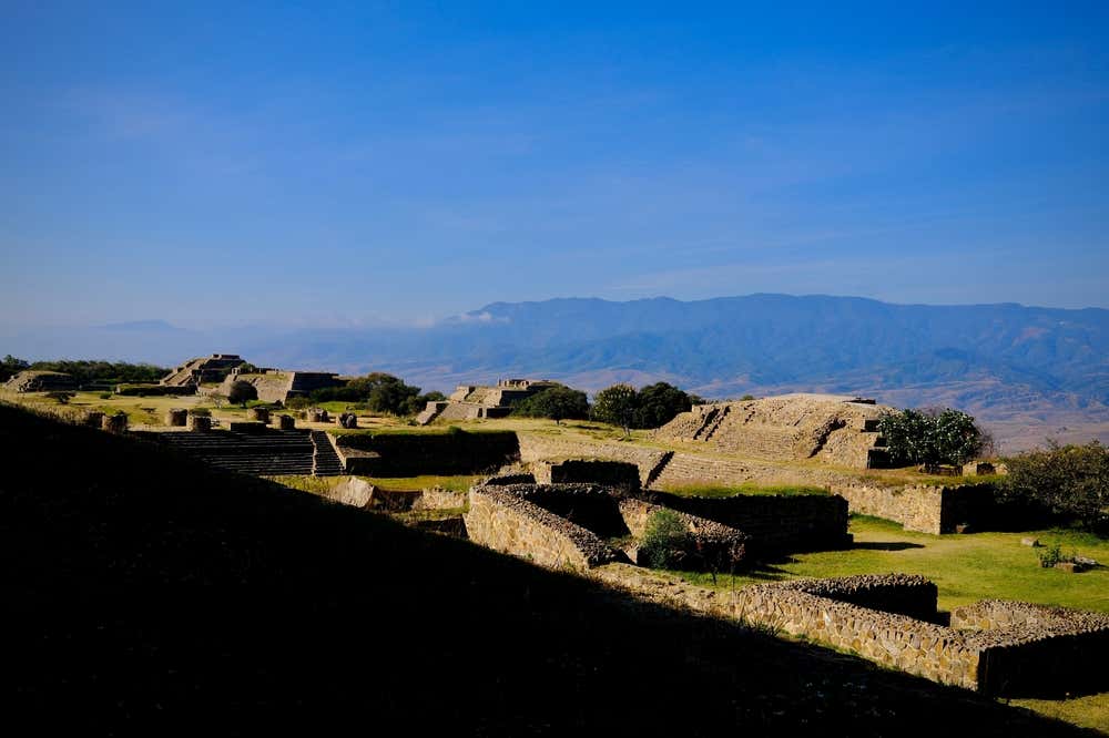 Monte Albán, Oaxaca with a large shadow on the left of the screen, and a clear blue sky in the background.
