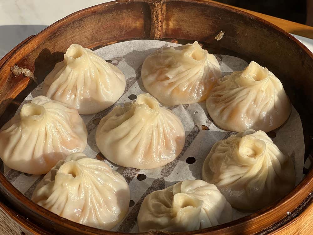 Vista dall'alto di un cestello di bambù per la cottura a vapore con all'interno otto xiaolongbao, i tipici ravioli cinesi ripieni di carne e brodo caldo con la loro caratteristica chiusura a pieghe in cima.