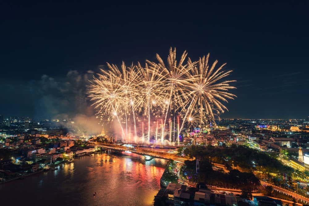 Fogos de artifício coloridos explodem sobre o rio Chao Phraya, com a ponte comemorativa e a paisagem urbana iluminada de Bangkok, na Tailândia