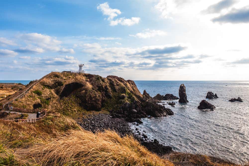 Paisagem de Seopjikoji, na ilha de Jeju, com o litoral rochoso, a vegetação e o mar compondo um cenário natural de grande beleza