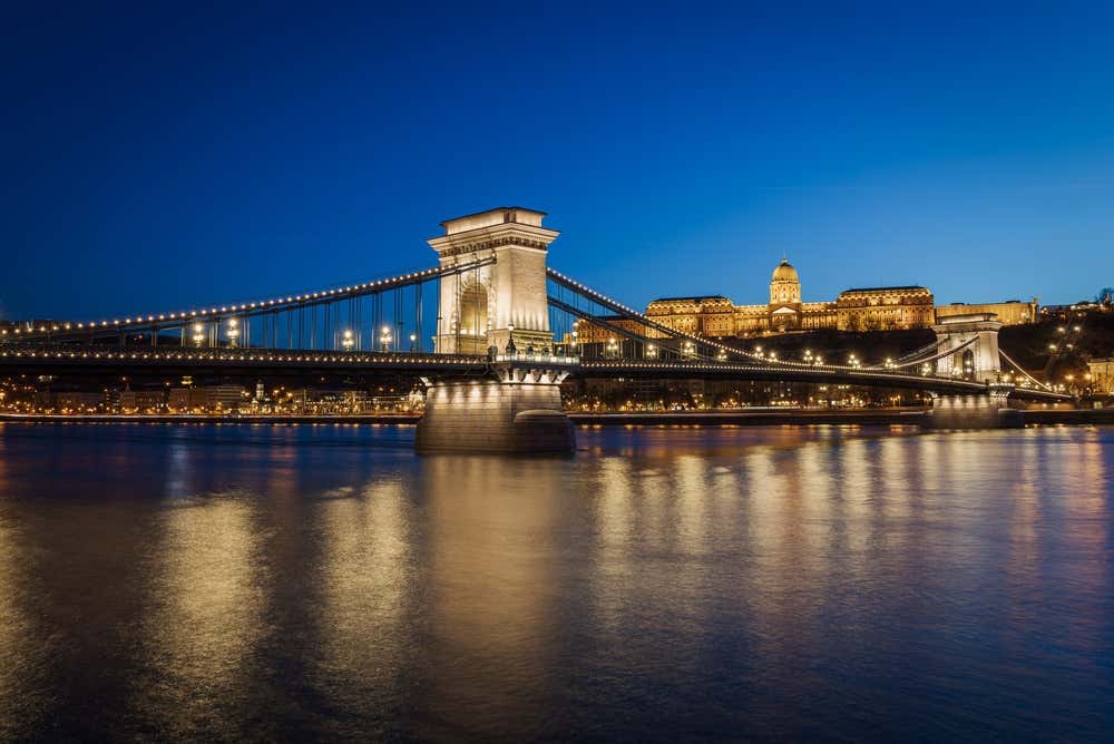 A Ponte das Correntes Széchenyi, em Budapeste, sobre o rio Danúbio à noite, com as luzes acesas e o Castelo de Buda ao fundo