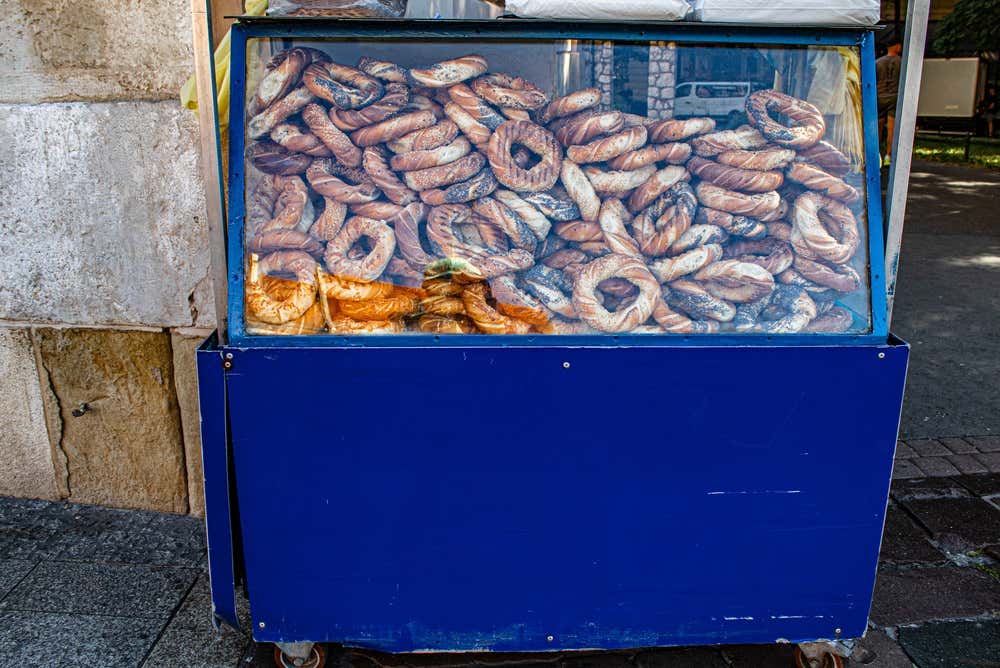 Un carretto blu da ambulante con vetrina colma di obwarzanek krakowski, i tipici panini intrecciati a ciambella coperti di semi di papavero e sesamo, posizionato su una strada di Cracovia