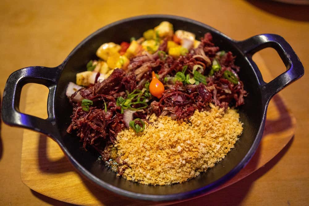 Baião de dois servido em panela de ferro, acompanhado de chips de mandioca crocantes. Um prato tradicional da culinária nordestina brasileira, preparado com arroz, feijão e ingredientes típicos da região