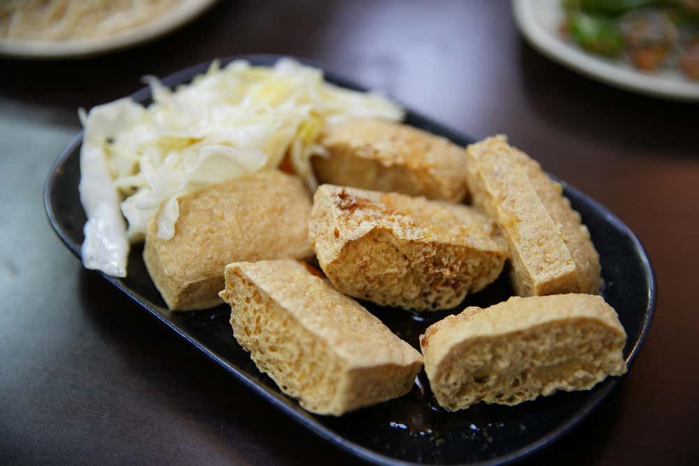 Piatto ovale nero contenente cubotti di tofu puzzolente fritto e croccante, accompagnati da un contorno di cavolo cappuccio fermentato in stile taiwanese