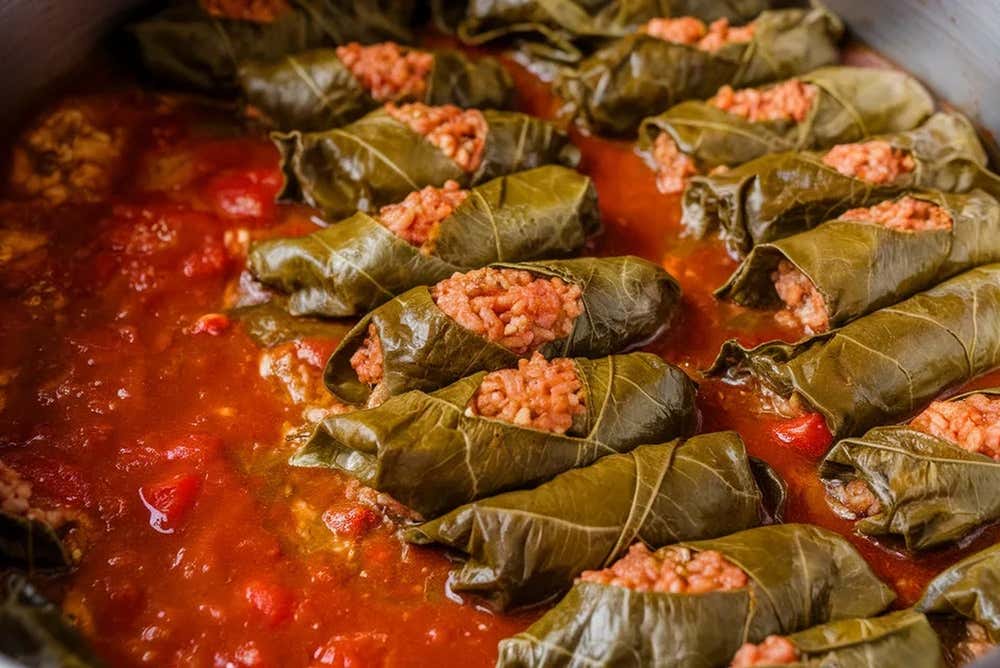 Involtini di foglie di vite (dolmades) ripieni di riso e carne al pomodoro, disposti ordinatamente all'interno di una pentola in cottura con salsa di pomodoro denso