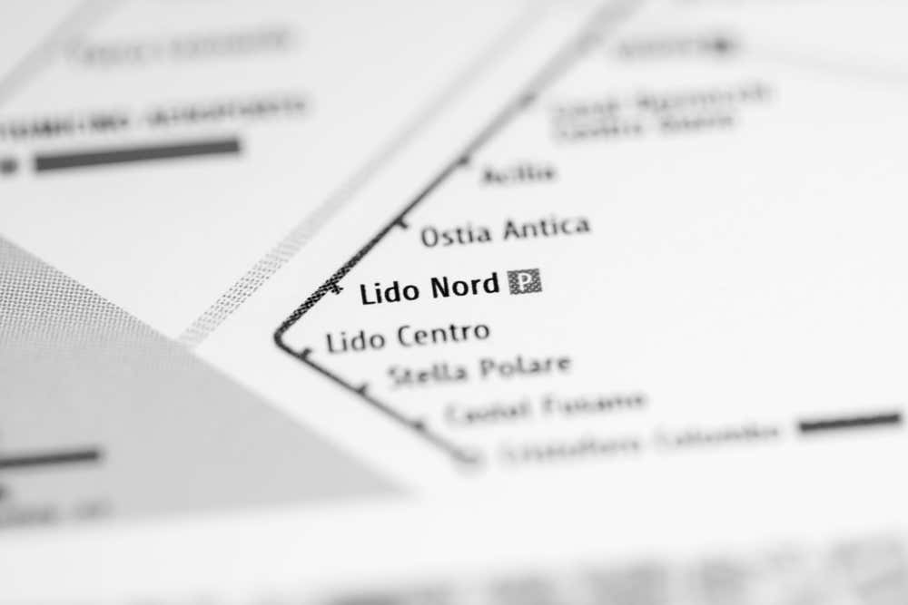 Primo piano macro della mappa della linea ferroviaria Roma-Lido, con il nome della stazione "Lido Nord" in evidenza e affiancato dall'icona del parcheggio "P", insieme ad altre fermate vicine come Ostia Antica, Lido Centro e Stella Polare