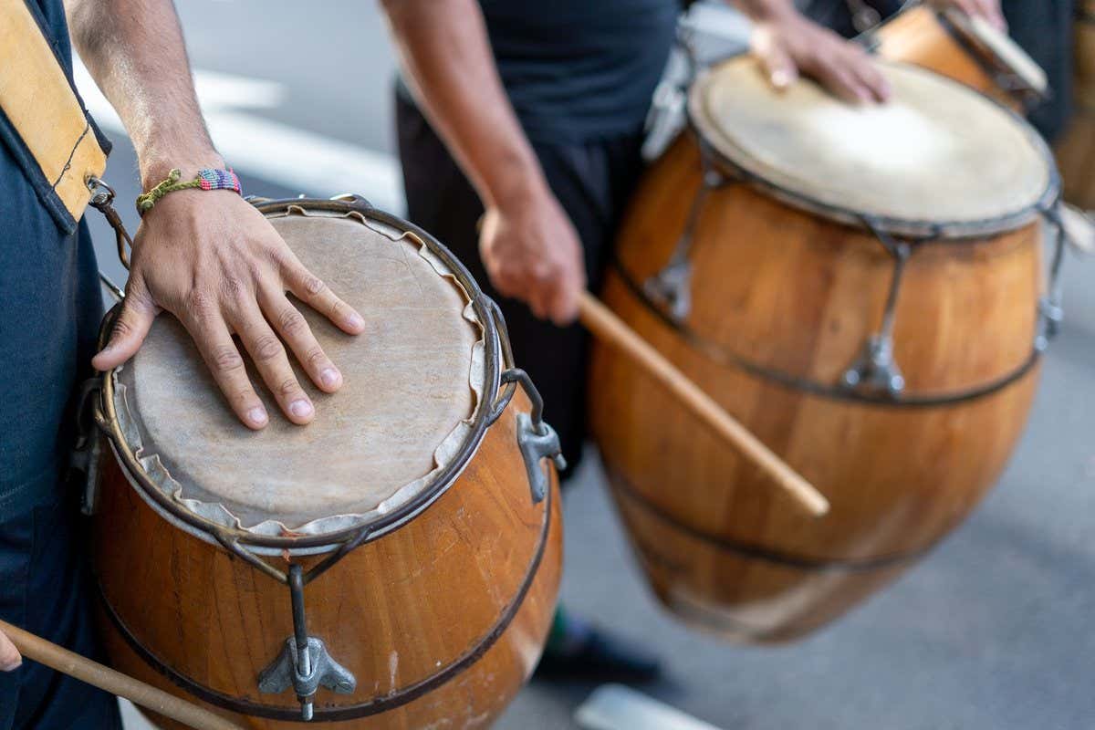 Manos tocando tambores de candombe de madera durante una celebración callejera en Buenos Aires