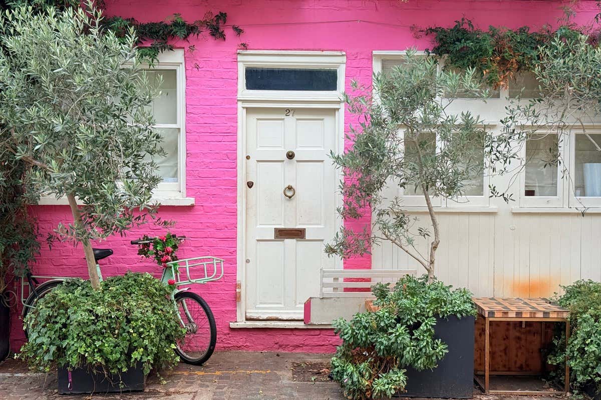 Fachada de tijolos rosa com porta branca e uma bicicleta em um beco do bairro de Notting Hill